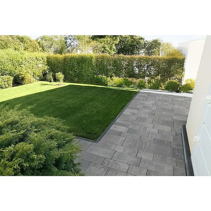 EHL EIBA Pflasterstein - 33 x 16,5 x 8 cm, Grau-Anthrazit, Beton - Die gepflasterte Terrasse führt zu einem grünen Rasen mit üppigen Büschen und einer hohen Hecke im Hintergrund. Eine moderne Gartengestaltung.