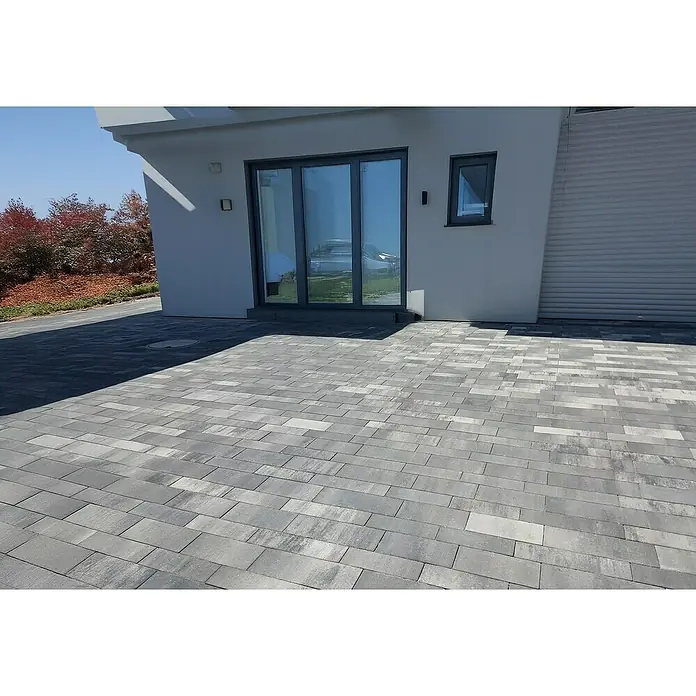 EHL Pflasterstein Tala Kombi - 125 x 83 x 8 cm, Weiß-Anthrazit, Beton, Gesamtstückzahl: 18 Stk. - Das Bild zeigt eine graue Pflastersteinoberfläche, die einen modernen Außenbereich mit einem Gebäude im Hintergrund gestaltet. Die Steine sind rechteckig und in einem versetzten Muster verlegt.