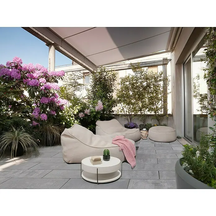 EHL Pflasterstein Cortona Flair - 60 x 30 x 8 cm, Grau-Anthrazit, Beton - Entspannende Outdoor-Szene mit bequemen Sitzsäcken, einem runden Tisch und üppigem Grün auf einer stilvollen Terrasse mit Steinboden.