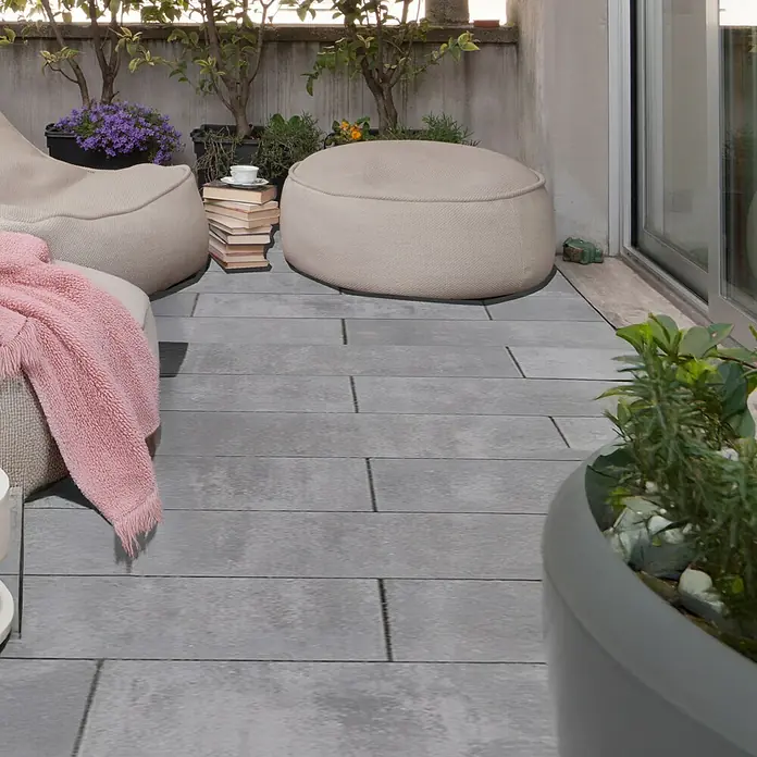 EHL Pflasterstein Cortona Flair - 60 x 30 x 8 cm, Grau-Anthrazit, Beton - Bequeme Sitzsäcke und graue Bodenfliesen auf einem gemütlichen Balkon mit Pflanzen und Büchern. Genießen Sie entspannte Stunden im Freien.