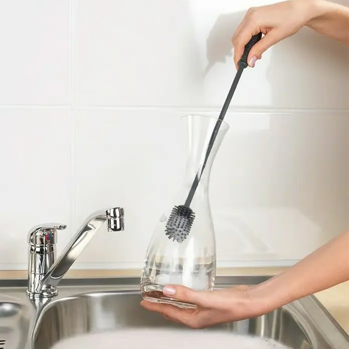 Wenko Spülbürste - Länge: 38 cm, Silikon - Eine Person reinigt eine Glaskaraffe mit einer Flaschenbürste am Spülbecken. Die Bürste hat einen langen Griff und einen runden Bürstenkopf.