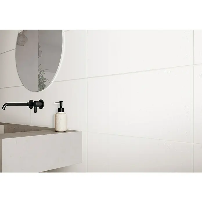 DryTile Wandfliese Palazzo Strukturiert Plast - 30 x 60 cm, Weiß, Matt - Nahaufnahme eines Waschbeckens mit einer schwarzen Armatur, einem runden Spiegel und einem Seifenspender vor einer weißen Wand mit Fliesen.