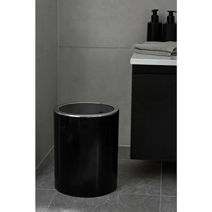 MSV Cubo de basura de baño Kamaka - 6 l, Plástico, Negro - Un elegante cubo de basura negro para baño con borde cromado se encuentra junto a un tocador oscuro con una toalla y dispensadores de jabón.