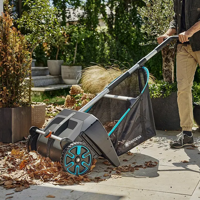 Gardena Nachrüstsatz - Passend für: Gardena Laub- & Rasensammler - Gardena Kehrmaschine mit Auffangkorb beim Aufsammeln von Laub auf einer Terrasse, umgeben von üppigem Grün.