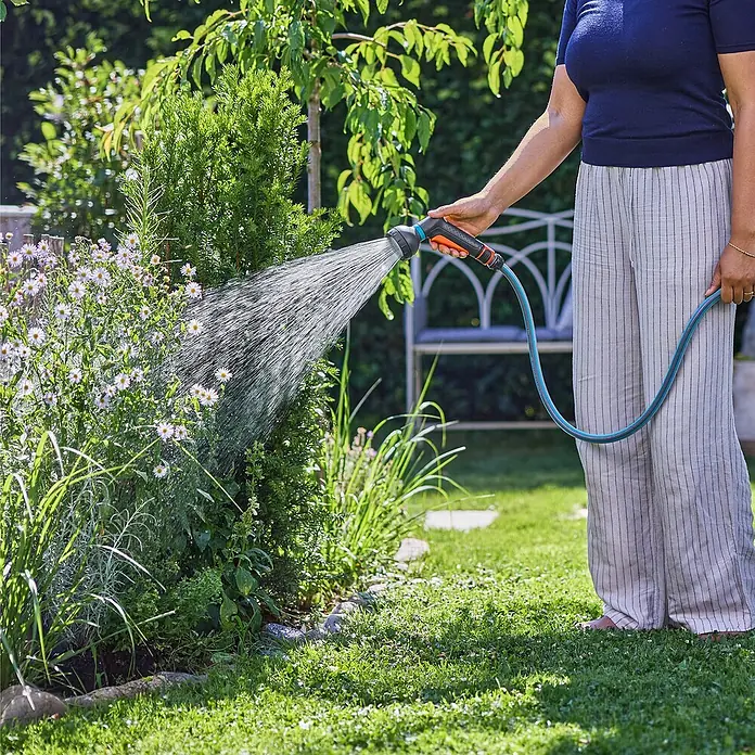 Gardena Classic Brausen-Set - 4 -tlg. - Eine Frau gießt mit einem Gardena-Bewässerungsaufsatz Blumen in ihrem Garten, während sie den Rasen grün und gesund hält.
