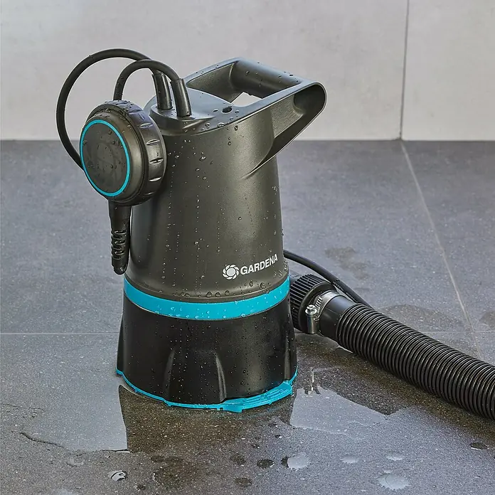 Gardena Schmutzwasserpumpe 20000 Basic Hochwasser-Set - 550 W, Max. Fördermenge: 20.000 l/h, Eintauchtiefe: 7 m - Das Bild zeigt eine Gardena Schmutzwasser-Tauchpumpe auf einem gefliesten Boden. Die Pumpe ist schwarz und blau und von Wassertropfen bedeckt.