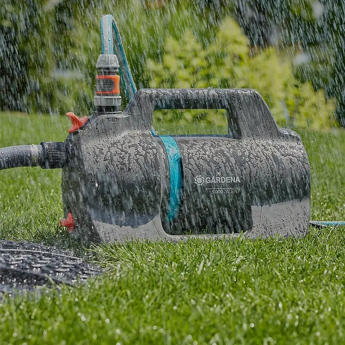 Gardena Gartenpumpen-Set 5000 Silent inkl. Gartenpumpe 5000 Silent inkl. Schlauch & Sauggarnitur - 550 W, Max. Fördermenge: 5.000 l/h - Gardena 5000 Silent Gartenpumpe im Einsatz, umgeben von fallendem Wasser, auf einem Rasen platziert.