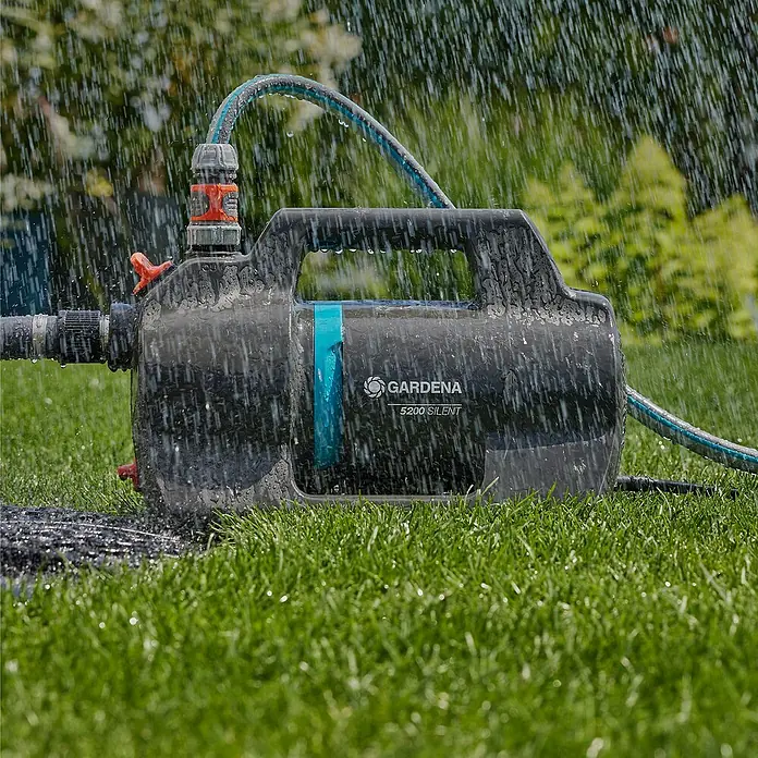 Gardena Gartenpumpe 5200 Silent - 600 W, Max. Fördermenge: 5.300 l/h - Die Gardena 5200 Silent Gartenpumpe unter der Bewässerung im Garten. Das Gerät ist kompakt, schwarz und blau und mit Schläuchen verbunden.