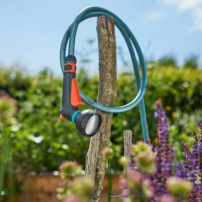 Gardena Classic Bewässerungsbrause - Weicher Brausestrahl, Kunststoff - Gartenspritze der Marke Gardena mit Schlauch, hängend an einem Holzpfosten, ideal für die Gartenbewässerung und Reinigung im Außenbereich.