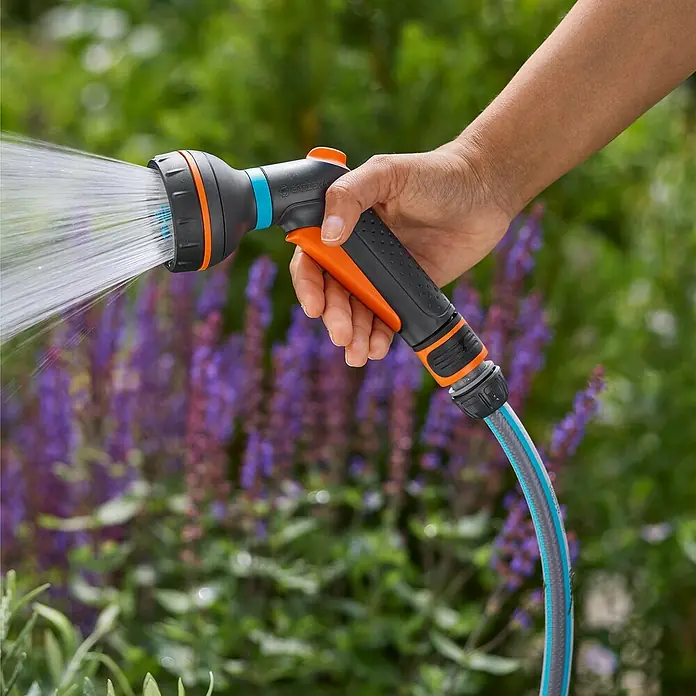 Gardena Classic Multibrause Starter-Set - Anzahl Sprühformen: 4 Stk., Kunststoff - Nahaufnahme einer Hand, die einen Gardena-Gartenschlauch mit Sprühkopf hält, der Wasser verspritzt.\n