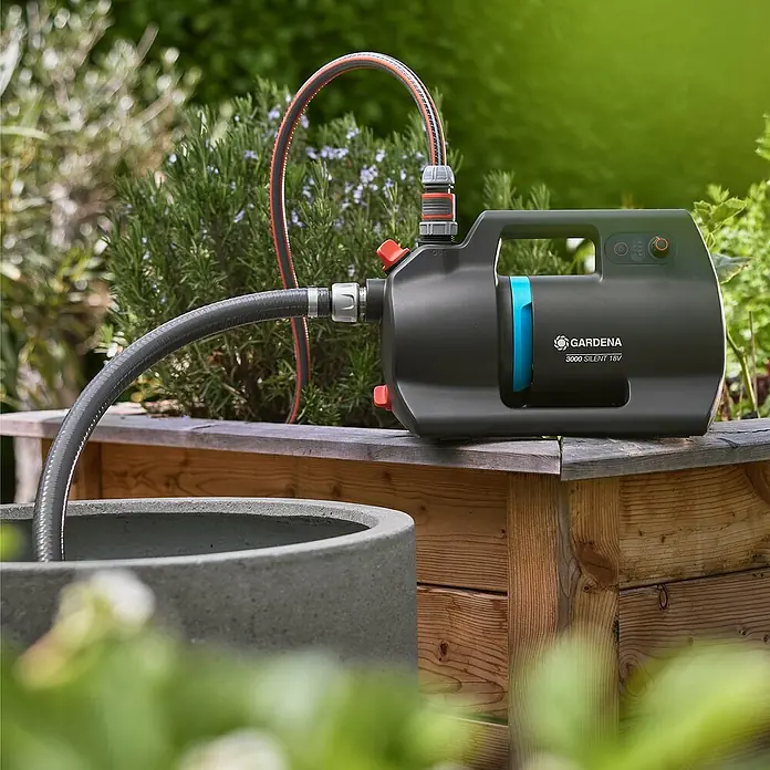Gardena Power for All 18V Akku-Gartenpumpe 3000 Silent - 18 V, Li-Ionen, 1 Akku, Max. Fördermenge: 3.000 l/h - Gardena 3000 Silent 18V Gartenpumpe mit angeschlossenen Schläuchen auf einer Holzerhöhung, bereit für die Gartenbewässerung.