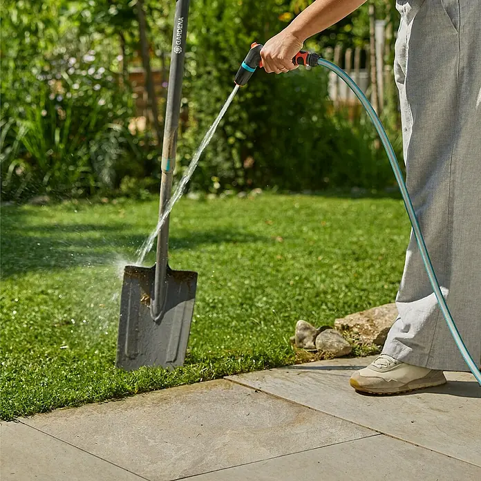 Gardena Classic Reinigungsspritze - Anzahl Sprühformen: 2 Stk., Kunststoff, Blau/Grau/Orange - Eine Person reinigt eine Gartenschaufel mit einem GARDENA-Sprühgerät vor einem grünen Rasen.