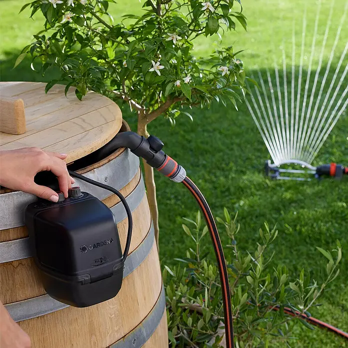 Gardena Power for All 18V Akku-Regenfasspumpe 2500 ComfortAutomatic - 1 Akku, Max. Fördermenge: 2.400 l/h - Der Gardena Regenfasspumpe mit Bewässerungssteuerung wird an einem Regenfass befestigt und ist mit einem Regner verbunden.