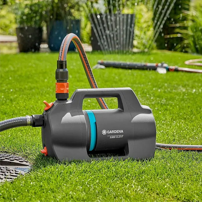 Gardena Gartenpumpe 5000 Silent - 550 W, Max. Fördermenge: 5.100 l/h - Eine GARDENA 5000 Silent Gartenpumpe mit angeschlossenen Schläuchen steht auf einem Rasen und bewässert den Garten.
