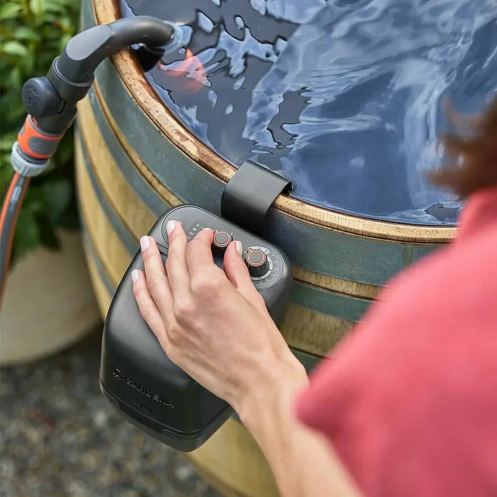 Gardena Power for All 18V Akku-Regenfasspumpe 2500 ComfortAutomatic - 1 Akku, Max. Fördermenge: 2.400 l/h - Nahaufnahme einer Person, die eine Gardena Bewässerungssteuerung an einem Wasserfass bedient, ideal für Gärten.