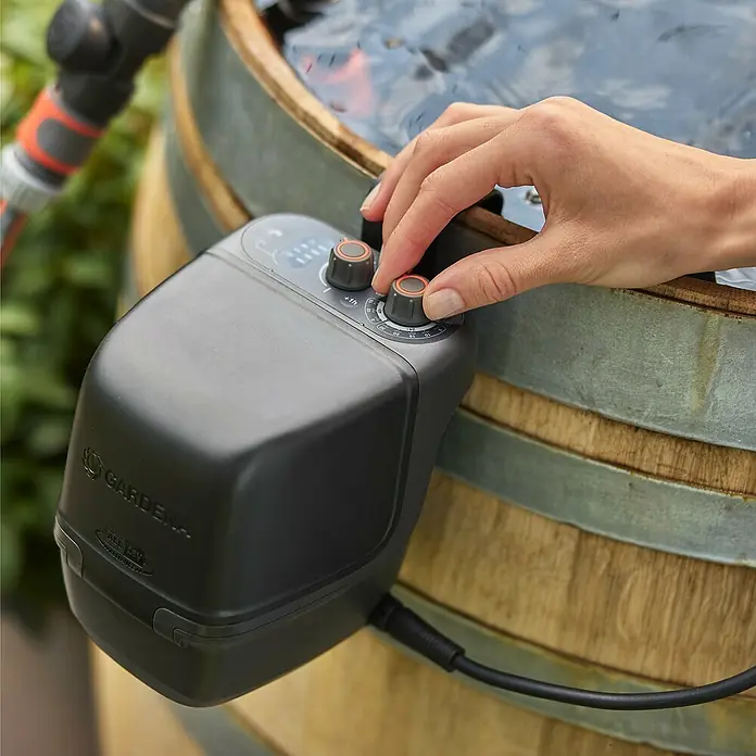 Gardena Power for All 18V Akku-Regenfasspumpe 2500 ComfortAutomatic - 1 Akku, Max. Fördermenge: 2.400 l/h - Nahaufnahme eines GARDENA Bewässerungscomputers am Wassertank, der von einer Hand eingestellt wird.