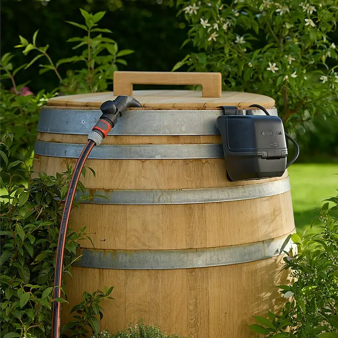 Gardena Power for All 18V Akku-Regenfasspumpe 2600 Comfort - Ohne Akku, Max. Fördermenge: 2.600 l/h - Das Bild zeigt eine Regentonne aus Holz mit einem Gardena Bewässerungsautomat. Ideal für die Gartenbewässerung mit Regenwasser.
