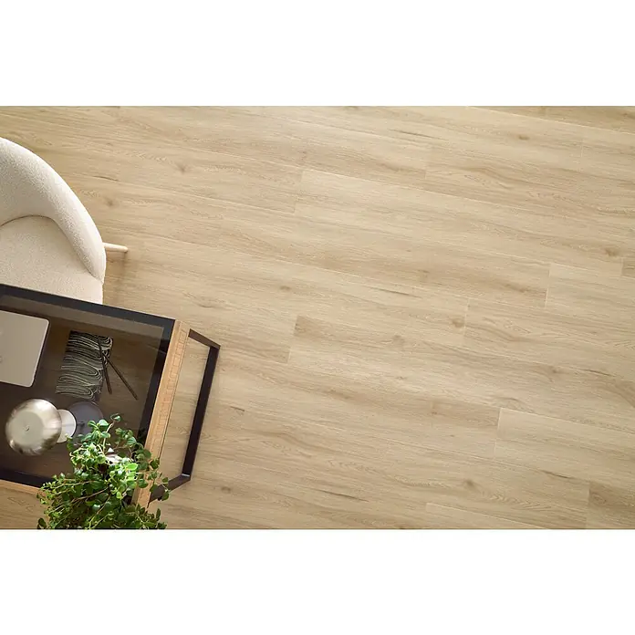 Vinylboden SPC XL - Eiche Harlow, Landhausdiele, 1.511 x 229 x 6,3 mm - Ansicht von oben auf ein modernes Wohnzimmer mit einem Couchtisch mit Glasplatte und einem cremefarbenen Sessel auf hellem Holzboden.