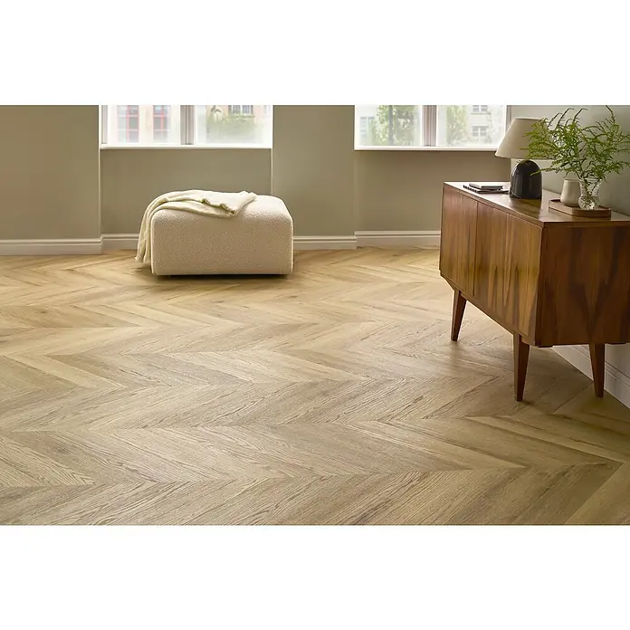 Vinylboden SPC Chevron - Tucson Eiche, 120 x 600 x 4,5 mm - Ein helles, modernes Wohnzimmer mit einem markanten Fischgrätparkettboden, einem cremefarbenen Hocker und einem Sideboard aus Holz.