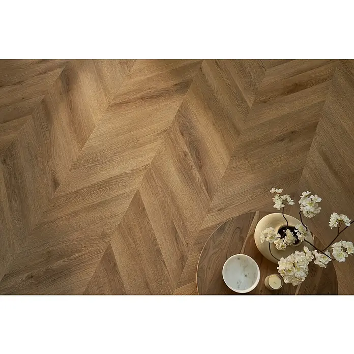 Vinylboden SPC Chevron - Garda Eiche, 120 x 600 x 4,5 mm - Detailaufnahme eines Raumes mit hellem Fischgrätparkett, auf einem Holztisch stehen Dekoartikel und Blütenzweige.