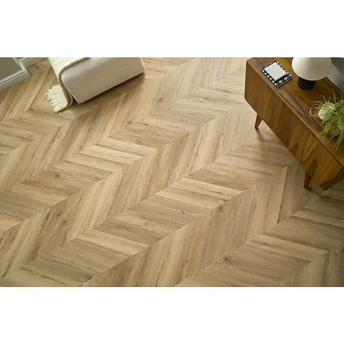 Vinylboden SPC Chevron - Tucson Eiche, 120 x 600 x 4,5 mm - Ein modernes Wohnzimmer mit hellen Holzböden im Fischgrätmuster, ergänzt durch einen Schrank und einen Hocker mit Decke.
