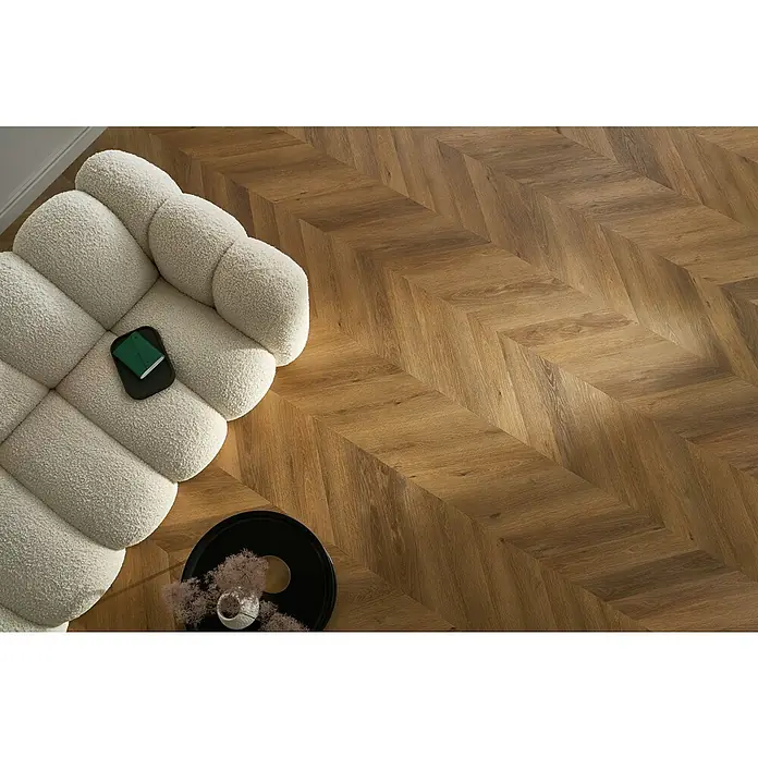 Vinylboden SPC Chevron - Frisco Eiche, 120 x 600 x 4,5 mm - Helles, modulares Sofa mit Kissen und dunklem Beistelltisch auf einem Holzboden in Fischgrätmuster.