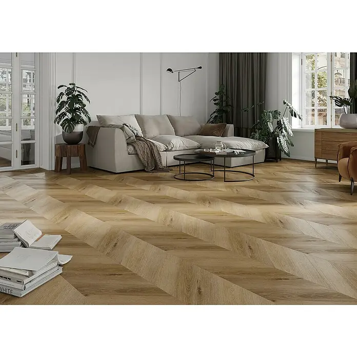Vinylboden SPC Chevron - Frisco Eiche, 120 x 600 x 4,5 mm - Einladendes Wohnzimmer mit markantem Fischgrätparkettboden in warmen Holztönen, das eine gemütliche Atmosphäre schafft.