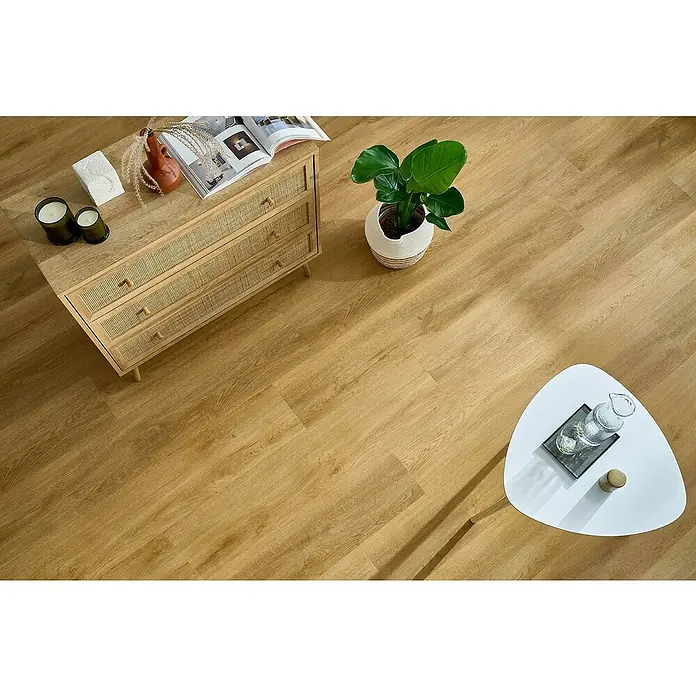 Vinylboden SPC XL - Eiche Sierra, Landhausdiele, 1.511 x 229 x 6,3 mm - Einladender Raum mit Kommode, Zimmerpflanze und weißem Tisch. Das warme Holzparkett verleiht dem Raum eine gemütliche Atmosphäre.