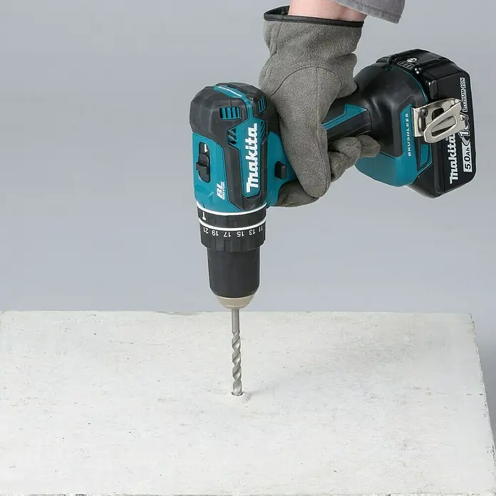 Makita LXT 18V Taladro percutor de batería DHP485 -  - Taladro inalámbrico de Makita perforando un agujero en una losa de hormigón, sujetado con un guante.