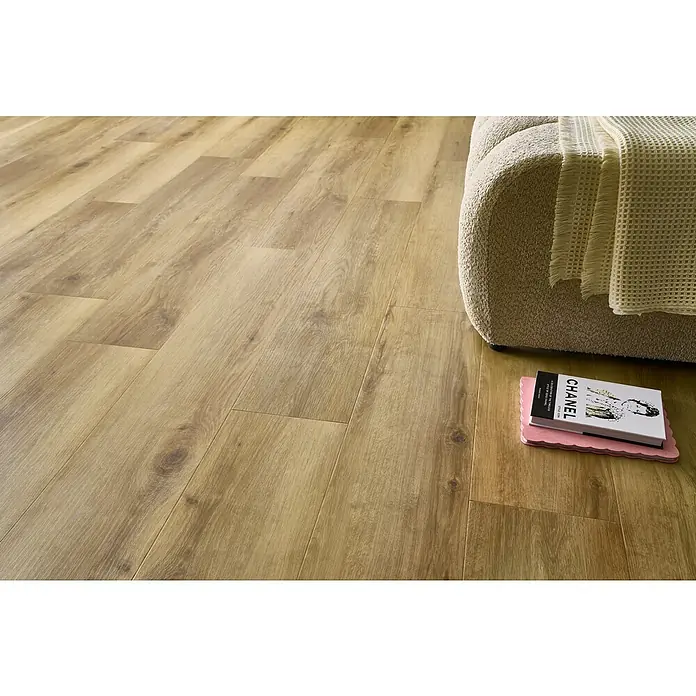 Vinylboden SPC Silent - Tucson Eiche, Landhausdiele, 1.220 x 229 x 5,3 mm - Nahaufnahme eines Holzfußbodens mit einem Buch, das auf einer Matte unter einem Möbelstück liegt.