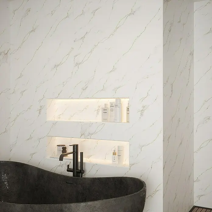 Wetwall Wandpaneel Elite - 16 x 242 cm, Bianco Carrara, Abgerundete Kante - Ein Badezimmer mit einer modernen schwarzen Badewanne und eingebauten Regalen mit Pflegeprodukten an einer Marmorwand.