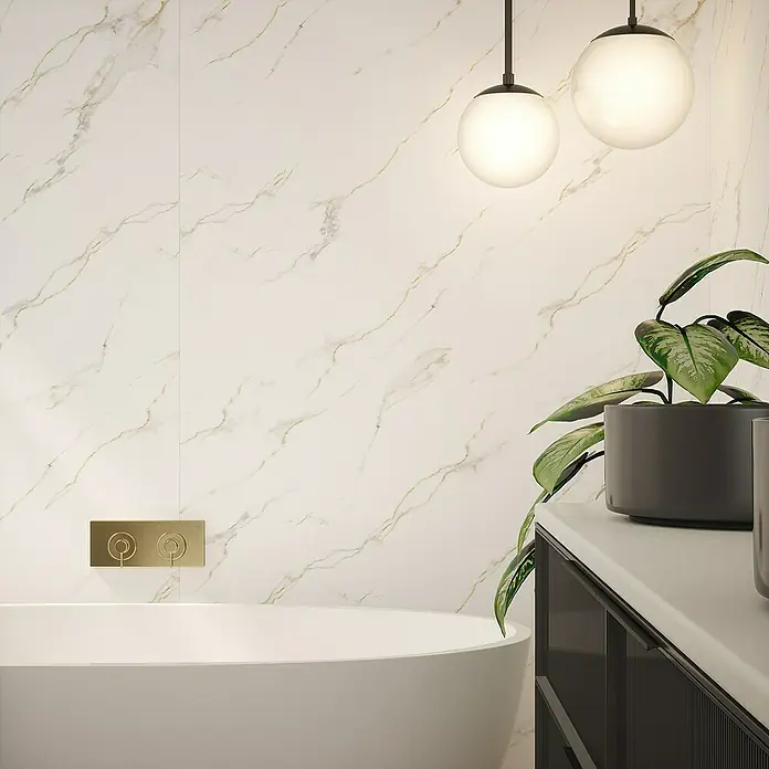 Wetwall Wandpaneel Elite - 16 x 242 cm, Bianco Carrara, Abgerundete Kante - Ein Badezimmer mit einer freistehenden Badewanne, stilvollen Leuchten und einer grünen Pflanze auf einem Waschtisch.