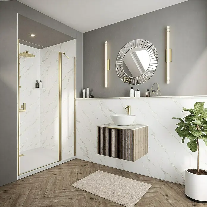 Wetwall Wandpaneel Elite - 16 x 242 cm, Bianco Carrara, Abgerundete Kante - Helles Badezimmer mit Marmorwänden, einer Dusche mit Goldrahmen und einem runden Spiegel über einem modernen Waschtisch.