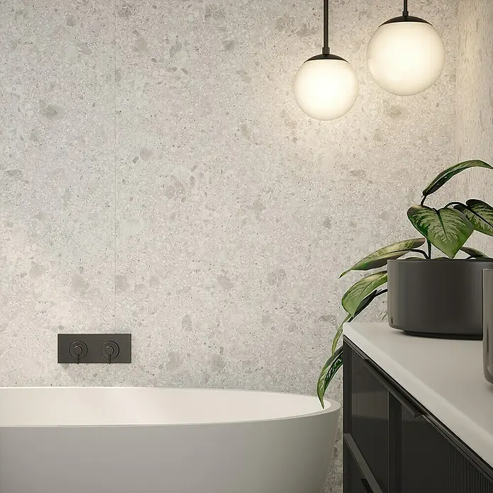 Wetwall Wandpaneel Elite - 16 x 242 cm, Terrazzo White, Abgerundete Kante - Elegantes Badezimmer-Design mit freistehender Badewanne, grauen Steinwandfliesen und stilvollen Hängeleuchten für eine moderne Atmosphäre.