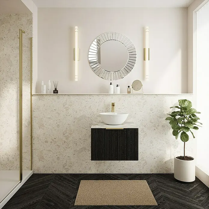 Wetwall Wandpaneel Elite - 16 x 242 cm, Terrazzo Rock, Abgerundete Kante - Elegantes Badezimmer-Interieur mit rundem Spiegel und stilvollem Waschbecken auf einem modernen, schwarzen Unterschrank. Eine grüne Pflanze sorgt für frische Akzente.