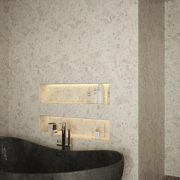 Wetwall Wandpaneel Elite - 16 x 242 cm, Terrazzo Rock, Abgerundete Kante - Nahaufnahme eines Badezimmers mit einer dunklen Badewanne und eingebauten Regalen, die mit Hautpflegeprodukten gefüllt sind.