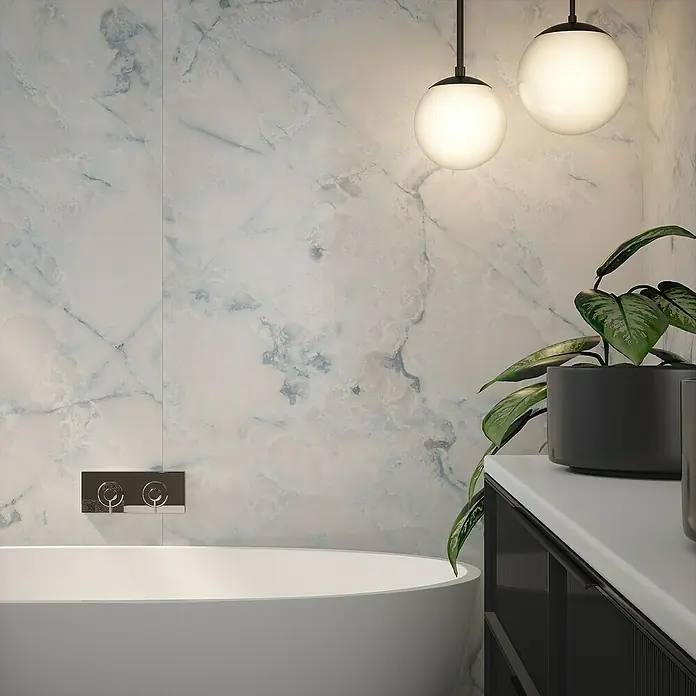 Wetwall Wandpaneel Elite - 16 x 242 cm, Onyx Oro, Abgerundete Kante - Elegantes Badezimmer mit einer freistehenden Badewanne vor einer marmorierten Wand, beleuchtet durch moderne Hängeleuchten und dekoriert mit einer Zimmerpflanze.