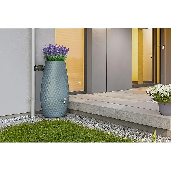 Garantia Regenspeicher Triagon 2 in 1 - 230 l, Agave, 1 Stk. - Grauer Regenspeicher im Garten mit Lavendel bepflanzt, an einer Hauswand platziert. Praktische und dekorative Wasserspeicherlösung.
