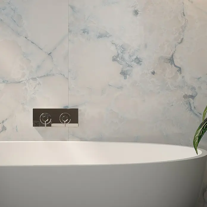 Wetwall Wandpaneel Elite - 16 x 242 cm, Onyx Oro, Abgerundete Kante - Nahaufnahme einer Badewanne mit Armaturen vor einer Wand mit Marmorstruktur. Die Badewanne ist weiß und hat eine ovale Form.