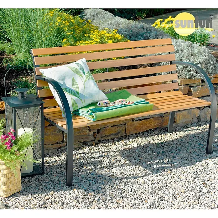 Sunfun Banco de jardín Saale - An x Pr x Al: 122 x 60 x 80 cm, Madera dura - Un elegante banco de jardín de madera y metal con cojín y manta, decorado con una linterna y una cesta de flores para un ambiente acogedor.