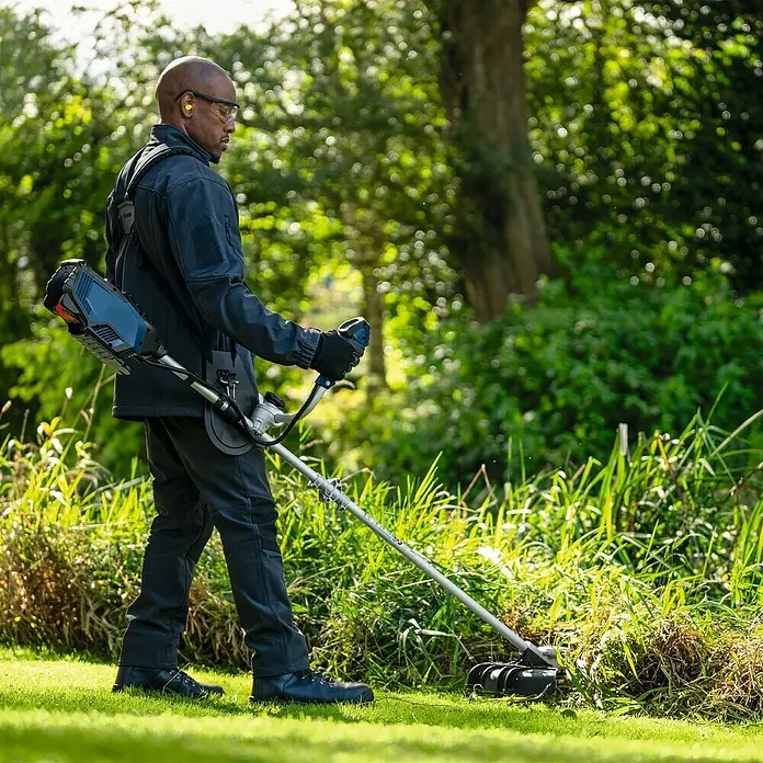 Bosch Professional AMPShare 18V Akku-Freischneider GFR18V-25 BH - 18 V, Schnittbreite Faden: 40 cm, Schnittbreite Messer: 25 cm - Ein Mann benutzt einen Rasentrimmer im Garten. Der Rasentrimmer von Bosch ist mit einem Akku ausgestattet, der auf dem Rücken getragen wird.