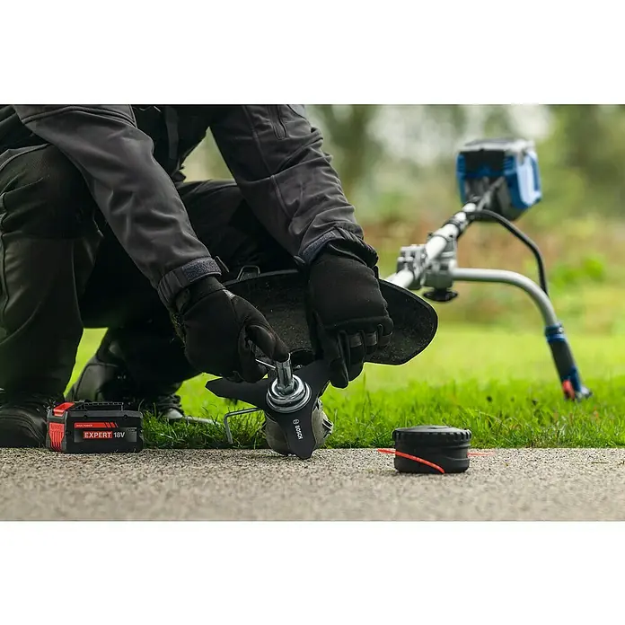 Bosch Professional AMPShare 18V Akku-Freischneider GFR18V-25 BH - 18 V, Schnittbreite Faden: 40 cm, Schnittbreite Messer: 25 cm - Nahaufnahme eines Mannes, der eine Bosch-Akku-Grasschere wartet, wobei der Fokus auf dem Schneidkopf und der Batterie liegt.