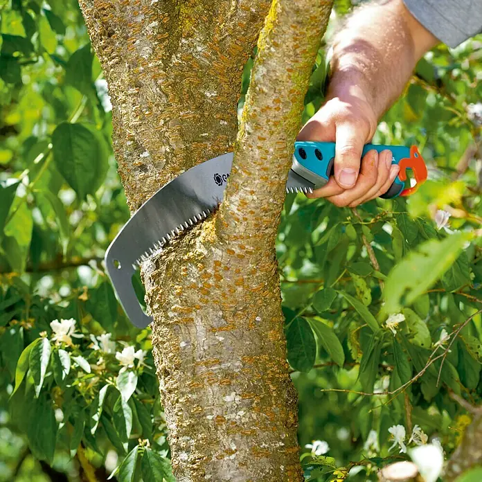 Gardena Combisystem Gartensäge 300 P gebogen - Sägeblattlänge: 34 cm - Das Bild zeigt eine Handsäge der Marke Gardena im Einsatz, die einen dicken Ast eines Baumes durchtrennt. Das Werkzeug liegt gut in der Hand.