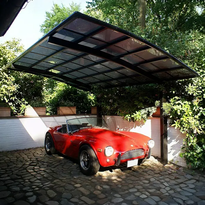 Ximax Carport PF60 - Außenmaß inkl. Dachüberstand (B x T): 2,7 x 4,95 m, Einzelcarport, Schwarz - Ein roter Oldtimer parkt unter einem modernen Carport mit transparentem Dach, umgeben von üppigem Grün. Schützt den Wagen vor Wettereinflüssen.