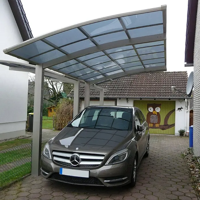 Ximax Carport PF60 - Außenmaß inkl. Dachüberstand (B x T): 3,01 x 5,56 m, Einzelcarport, Edelstahl-Look - Ein graues Mercedes-Benz Auto, das unter einem Carport mit einer durchsichtigen Überdachung parkt, vor einem Haus mit einer bemalten Garagentür.