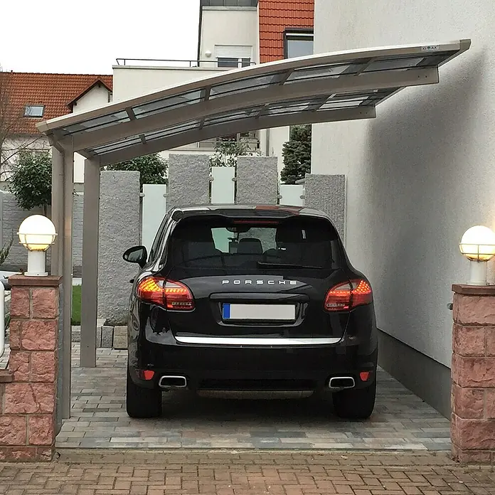 Ximax Carport PF60 - Außenmaß inkl. Dachüberstand (B x T): 3,01 x 5,56 m, Einzelcarport, Edelstahl-Look - Das Bild zeigt ein schwarzes Porsche SUV geparkt unter einem Carport mit silbernem Rahmen und transparentem Dach, umgeben von Steinpfosten und Lichtern.