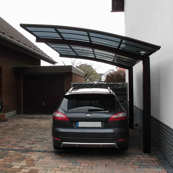 Ximax Carport Portoforte Typ 80 - Außenmaß inkl. Dachüberstand (B x T): 3,01 x 5,56 m, Einzelcarport, Mattbraun - Eine graue Ford Mondeo unter einem eleganten Carport mit dunklem Rahmen und transparentem Dach auf einem gepflasterten Hof.