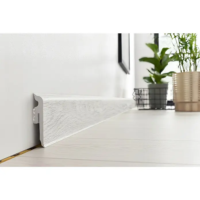 Sockelleiste Vigo - 220 x 1,5 x 6 cm, Takeda Eiche - Nahaufnahme einer weißen Sockelleiste an einer Wand, die das saubere und moderne Design mit Holzmuster hervorhebt.