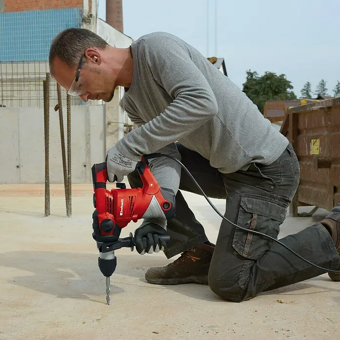 Einhell Kombihammer TC-RH 1600 - 1.600 W, 4 J, SDS-Plus-Aufnahme - Ein Mann kniet und bohrt mit einer roten Einhell Schlagbohrmaschine in Beton. Er trägt Schutzkleidung für sicheres Arbeiten.