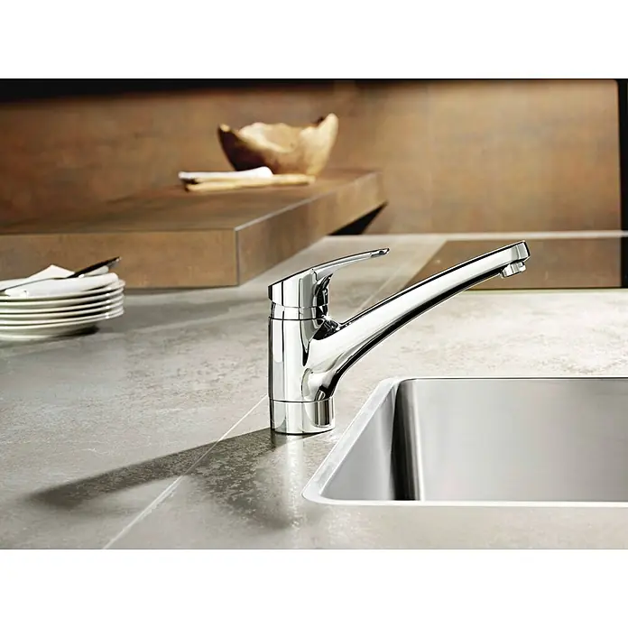 Hansa Mix Spültischarmatur - Chrom, Glänzend - Detailaufnahme eines glänzenden Chrom-Wasserhahns neben einem Spülbecken, Geschirr im Hintergrund. Hochwertiges Küchendesign mit moderner Armatur.